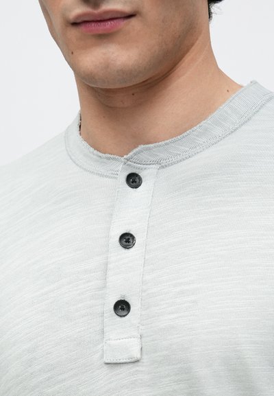 Jasnoszara koszula henley wykonana z teksturowanej tkaniny, charakteryzująca się okrągłym kołnierzykiem, trzema czarnymi guzikami oraz wykończeniem hemu z przeszyciem.