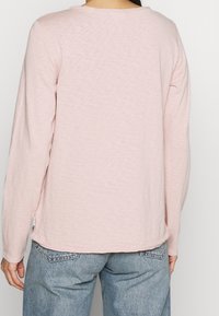 Ljusrosa långärmad tröja med rund halsringning, mjukt texturerat tyg och sidsprund, kombinerad med blå denimjeans.