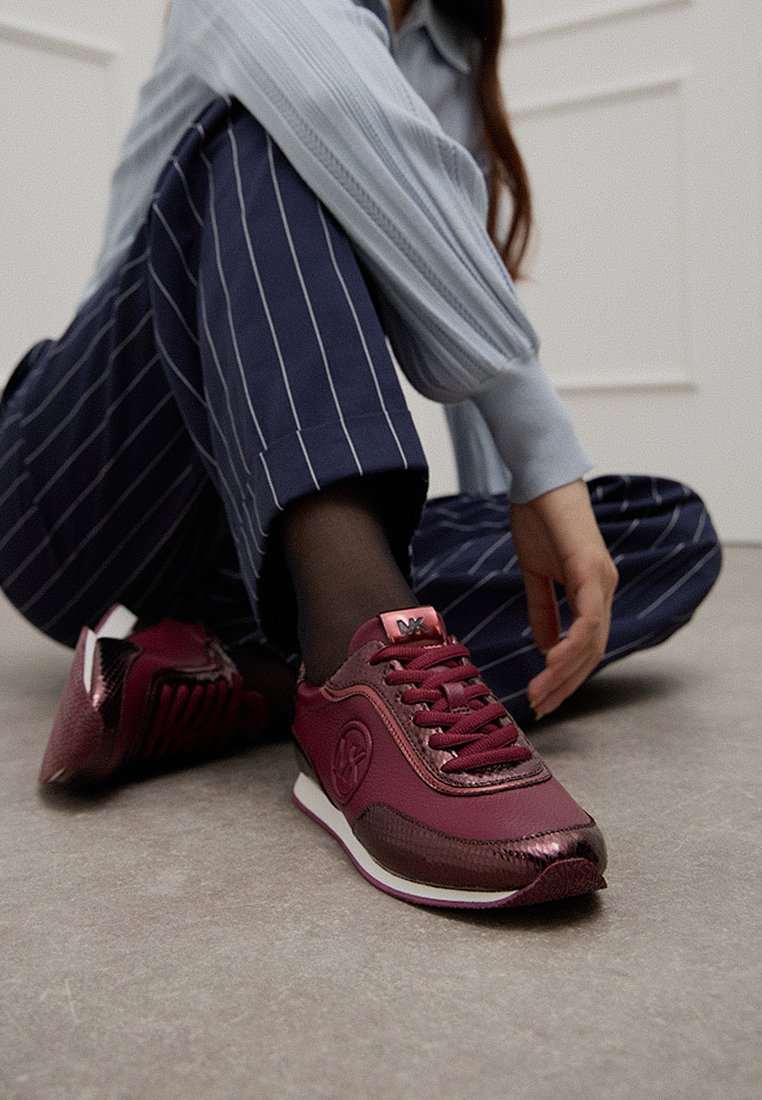 Sneakers bordeaux con tomaia in pelle liscia, dettagli testurizzati e suola bianca. Presentano lacci rotondi e un logo sul lato.