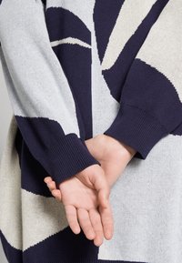 Maglione lavorato a maglia con pattern geometrico in blu navy, crema e grigio, con polsini a coste e vestibilità rilassata, che mette in evidenza una texture morbida.