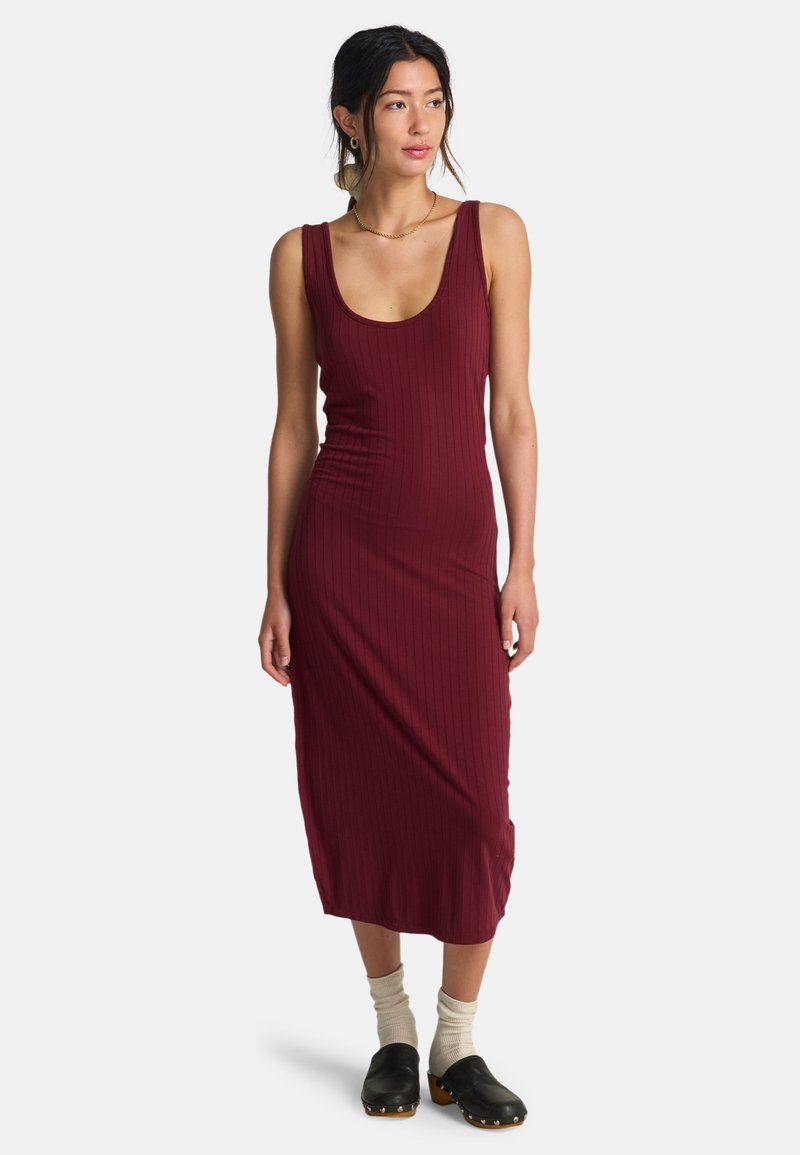 Μωβ μίντι ριμπ φόρεμα με στρογγυλή λαιμόκοψη, εφαρμοστή σιλουέτα και πλαϊνές σκισμές, συνδυασμένο με μαύρα ξύλινα παπούτσια και ανοιχτόχρωμες κάλτσες.