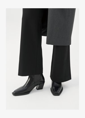 Stivali alla caviglia neri con punta quadrata e tacco affusolato, realizzati in pelle lucida con dettagli a righe verticali sui lati.