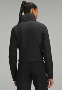 Melnā sporta jaka ar augstu apkakli, ar teksturētu aizmuguri un pieguļošām piedurknēm. Izgatavota no viegla, ūdensizturīga materiāla.