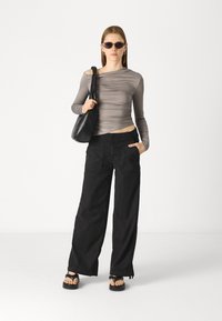 Gray long-sleeve top with gathered texture, black wide-leg pants with pockets, black sandals, and a black shoulder bag. Sunglasses worn.