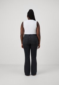 Svarte utvidede jeans med baklommer og en hvit tettsittende tanktopp. Materialet ser ut som denim; teksturen er glatt og lett slitt.