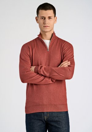 Pullover rosso a maniche lunghe con colletto a zip a un quarto, realizzato in tessuto morbido. Presenta polsini e orlo a costine, abbinato a jeans di denim blu scuro.