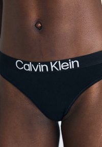 Sorte bomullsbikiniundertøy med bred elastisk midjebånd med hvit "Calvin Klein"-logo. Glatt tekstur og tettsittende design.
