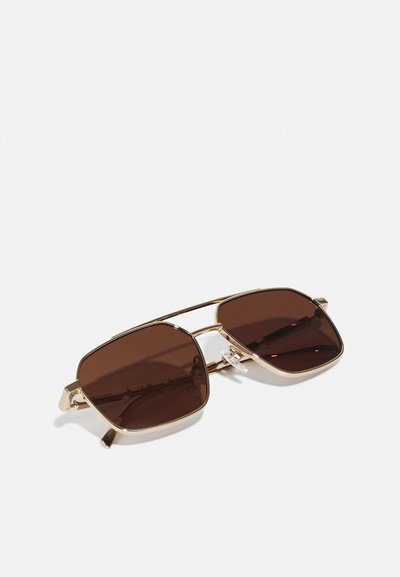 Gafas de sol con lentes marrones y montura de metal dorado, forma cuadrada, diseño de doble puente y almohadillas nasales transparentes. Textura suave y hardware mínimo.