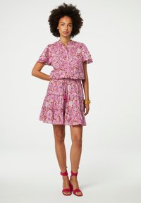 Rosenblumenmuster-Kleid mit Rüschensleeves, elastischem Taillenband und gestuftem Rock. Getragen mit pinkfarbenen Riemchen-Heels und goldenen Armreifen.