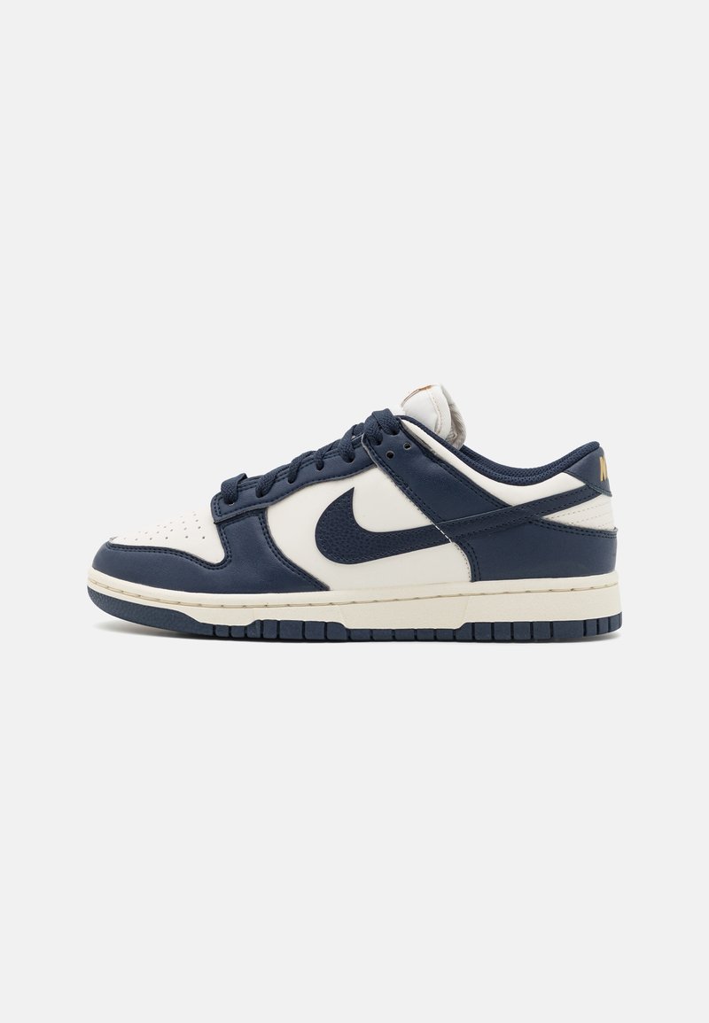 Marineblauwe en witte Nike Dunk sneakers hebben een gladde leren bovenkant met een geperforeerde neus, een contrasterende marineblauwe swoosh en een gestructureerde zool.