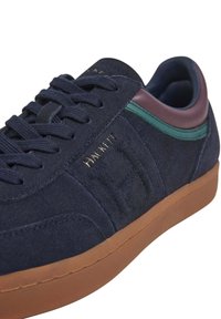 Zapatillas de gamuza en color marino con suela marrón, acentos en verde y burdeos, cordones también en color marino y la marca "Hackett" grabada en el lateral.