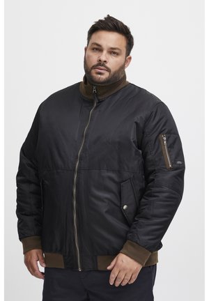 Chaqueta bomber negra con cremallera frontal, acentos marrones y un cuello alto. Presenta dos bolsillos laterales y un bolsillo adicional con cremallera en la manga.