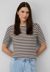 T-shirt rayé présentant des bandes horizontales marron et blanches, à manches courtes, avec un col rond et en coton doux. Associé à un jean bleu clair.