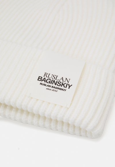 Biała, prążkowana czapka beanie z etykietą oznaczoną "Ruslan Baginskiy", z czarnym napisem. Miękka tekstura i elastyczny kształt, zaprojektowana do ścisłego dopasowania.
