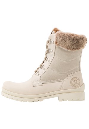 Bottine beige clair avec une doublure en fourrure douce, une tige en suède texturé, des œillets en métal et une semelle crème robuste. Détail du logo sur le côté.