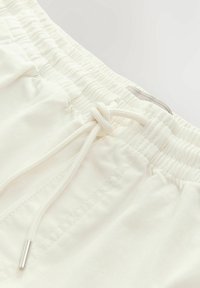 Shorts taille élastique beige clair avec cordon de serrage, présentant une texture lisse et des détails cousus sur les côtés.