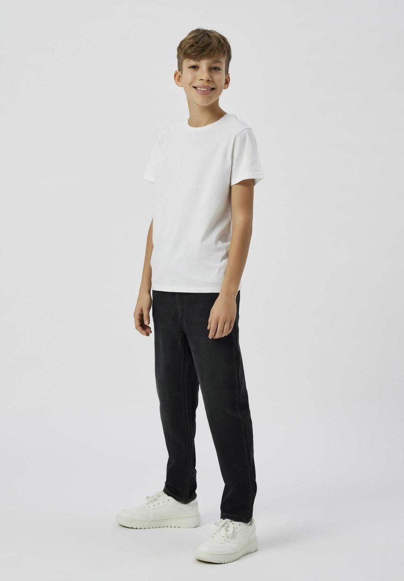 Camiseta blanca de manga corta combinada con pantalones vaqueros negros y zapatillas blancas. La parte superior tiene cuello redondo y los pantalones tienen un corte recto.