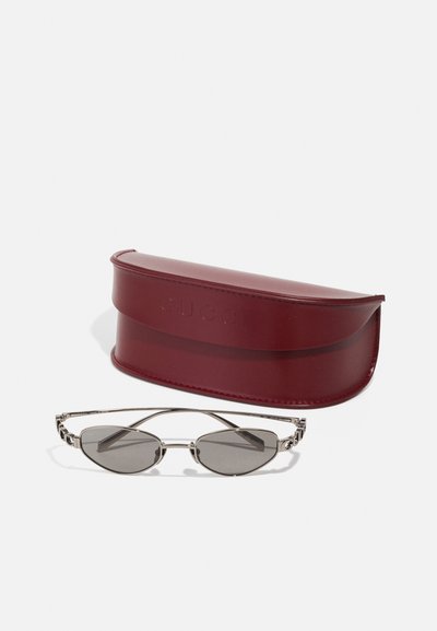 Ochelari de soare Gucci cu lentile gri elongate, ramă din metal argintiu și detalii complicate pe laterale. Include un toc din piele burgund.