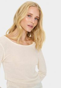 Cremefarbenes Langarmshirt mit weitem Ausschnitt und weichem, strukturiertem Stoff. Das Design beinhaltet lange Ärmel und eine lockere Passform.