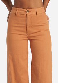 Pantaloni palazzo in cotone arancione, caratterizzati da una vita alta, chiusura con bottone e design minimalista. Tessuto liscio senza motivi.