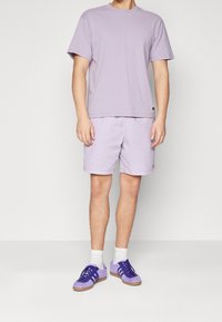 Světle fialové bavlněné tričko v kombinaci s odpovídajícími šortkami. Doplněno bílými ponožkami a fialovými teniskami se třemi pruhy a semišovými detaily.