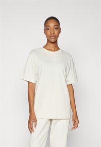 Lys beige bomulds t-shirt med korte ærmer, rund halsudskæring og et lille hvidt Puma-logo på brystet. Glat tekstur og afslappet pasform.