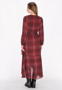 Lang rood geruite jurk met lange mouwen, gerende zoom en een cinched taille. Gekleed met zwarte enkellaarsjes, die een transparante stof toont.