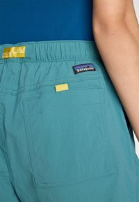 Calções turquesa com um cós elástico e um detalhe amarelo. Apresentam um bolso traseiro e um rótulo da marca Patagonia no canto superior direito.