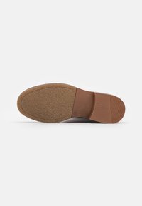 Suela de zapato marrón con caucho texturizado para agarre, presenta un tacón plano y bordes lisos, diseñado para durabilidad y comodidad.