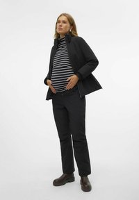 Veste noire sur un haut rayé noir et blanc, associée à un pantalon noir et des bottes marron. Présente une coupe décontractée et une texture lisse.
