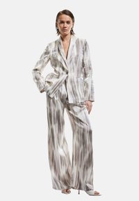 Ensemble de costume avec un motif à rayures de couleur claire en tons de gris et beige, comprenant un blazer ajusté et un pantalon à jambes larges. Tissu texturé.