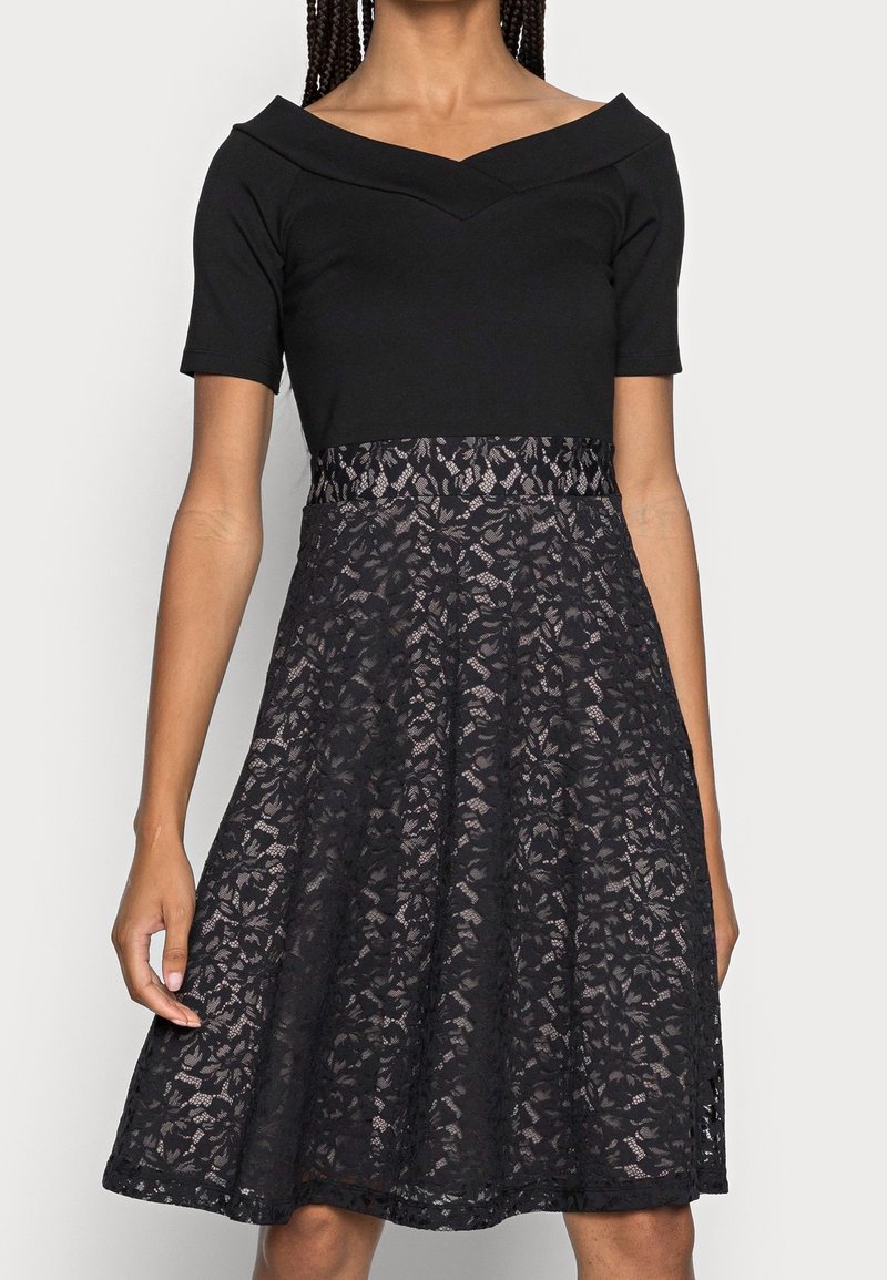 Černé šaty s krátkými rukávy, s přiléhavým živůtkem a rozšířenou krajkovou sukní. Krajka má květinový vzor a texturovaný povrch.
