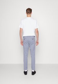 Grå bomullsbyxor med skräddarsydd passform, två bakfickor och svarta knappar, kombinerade med en enkel vit T-shirt och svarta skor.