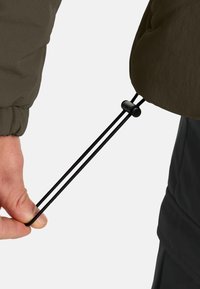De manchet van een groene nylon jas met een zwarte elastische trekkoord vastgehouden door een hand. Het trekkoord heeft een plastic versteller om aan te trekken.