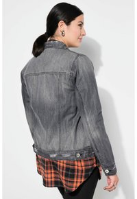 Farkkutakki haalistuneessa harmaassa, jossa on takasaumapisteitä, musta ja oranssi ruudullinen kerros alla ja metalliset napsautusnapit.