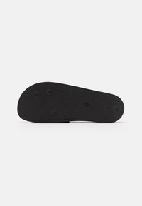 Black rubber shoe sole with a textured surface, featuring circular grip patterns and a smooth front edge.