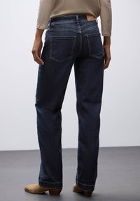 Jeans in denim blu scuro con taglio dritto, due tasche posteriori e un'etichetta in pelle sulla vita. Il tessuto ha una texture liscia.
