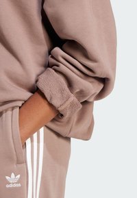 Felpa marrone con polsini a costine, che presenta un accento in maglia testurizzata sulle maniche. Strisce verticali bianche sui pantaloni abbinati.