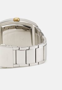 Silver stainless steel watch with a rectangular face, gold crown, and linked bracelet design. Features a polished texture and engraved logo.