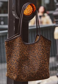 Brown and black leopard print tote bag hanging from an amber traffic signal on a street pole.