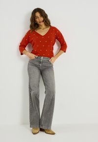 Suéter rojo de manga larga con patrones de corazones dorados y cuello en V, combinado con jeans gris acampanados y botines color canela con tacón.