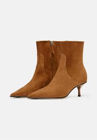 Botas de tobillo de ante marrón con punta afilada, caña corta y tacón de gato. Cuentan con un cierre lateral y una textura suave.