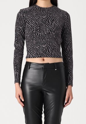 Kobieta ubrana w czarno-szary crop top w zebrę z długim rękawem, zestawiony z wysokim stanem czarnymi skórzanymi spodniami, stojąca na tle szarego tła.