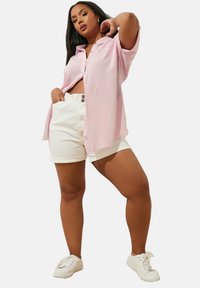 Ljusrosa skjorta med korta ärmar, kombinerad med högmidjade vita bomullsshorts. Utfinad med vita sneakers.