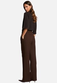 Pantalons marron à jambe large avec une coupe ajustée, présentant une texture lisse et des poches latérales. Associés à un haut noir ajusté et des accessoires minimalistes.