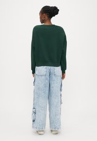 Grüner übergroßer Pullover mit rundem Ausschnitt, kombiniert mit hellblauen Cargo-Jeans mit mehreren Taschen und legerer Passform.