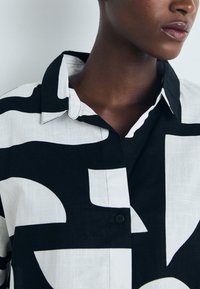 Camisa de botones en blanco y negro con patrones abstractos audaces, un cuello estructurado y una tela texturizada.