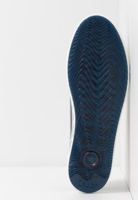 Semelle d'une basket bleu foncé avec un motif ondulé, une prise circulaire près du talon et le logo "Gabor" en bas.