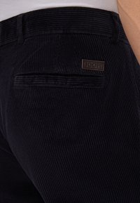 Donkerblauwe corduroy broek met een geribbelde textuur, voorzien van een achterzak en een klein bruin "JOOP!" label.