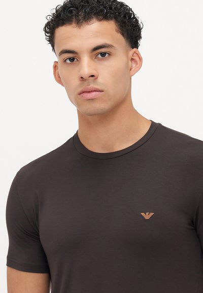 T-shirt castanho ajustado em tecido suave com decote redondo, mangas curtas e um pequeno logótipo laranja no lado esquerdo do peito.